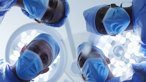 Portrait-of-diverse-surgeons-standing-in-operating-theatre-looking-at-patient-from-above