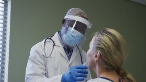 Diverse-female-patient-and-doctor-wearing-face-mask-doing-covid-swab-test