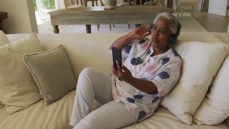 Lächelnde-Afroamerikanische-Seniorin-Mit-Kopfhörern,-Die-Zu-Hause-Einen-Videoanruf-Auf-Dem-Smartphone-Führt