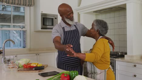 Pareja-De-Ancianos-Afroamericanos-Usando-Delantales-Bailando-Juntos-En-La-Cocina-De-Casa