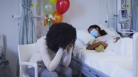 Stressed-african-american-mother-sitting-besides-her-her-daughter-lying-on-bed-at-hospital