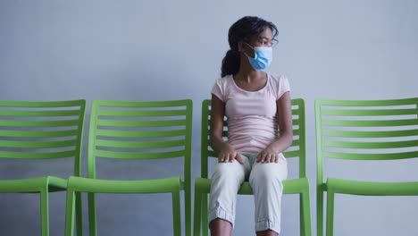 African-american-girl-wearing-face-mask-sitting-on-a-chair-at-hospital