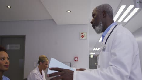 Diverse-male-doctor-at-hospital-reception-and-talking-to-female-staff