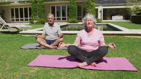 Glückliches-Kaukasisches-Seniorenpaar,-Das-Yoga-Praktiziert-Und-Im-Garten-In-Der-Sonne-Meditiert