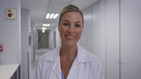 Portrait-of-caucasian-female-doctor-standing-in-corridor-laughing-looking-at-camera