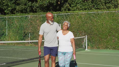 Pareja-De-Ancianos-Afroamericanos-Sosteniendo-Raquetas-Caminando-En-La-Cancha-De-Tenis