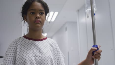 Mixed-race-girl-walking-with-drip-bag-in-hospital-room