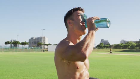 Fit-shirtless-caucasian-man-dinking-water-after-exercising-outdoors