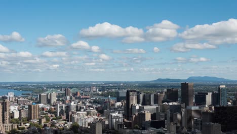 Modern-cityscape,-mountains-and-water-with-multiple-white-clouds-on-blue-sky-in-background