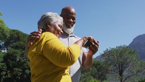 Happy-senior-african-american-couple-using-smartphone-taking-selfie-in-sunny-garden