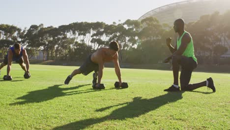 Diverse-group-of-three-fit-men-cross-training-doing-press-ups-with-weights-outdoors