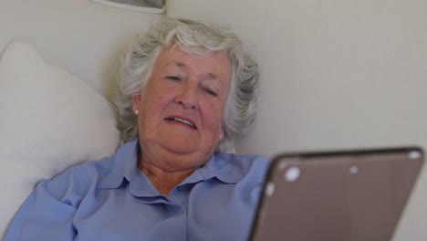 Kaukasische-Seniorin-Benutzt-Digitales-Tablet,-Während-Sie-Zu-Hause-Auf-Der-Couch-Liegt