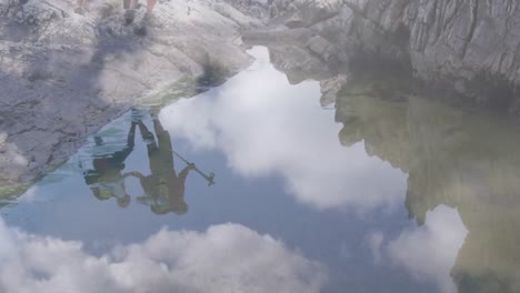 Caucasian-senior-couple-hiking-on-rocks-reflected-in-water,-over-fast-moving-clouds