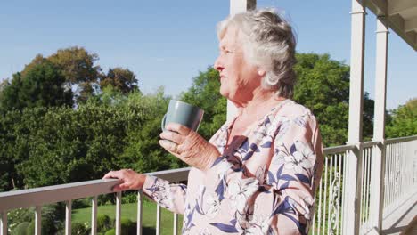Nachdenkliche-Kaukasische-Seniorin-Trinkt-Kaffee,-Während-Sie-Zu-Hause-Auf-Dem-Balkon-Steht