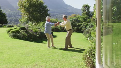 Happy-caucasian-senior-couple-dancing-together-in-the-garden-on-a-bright-sunny-day