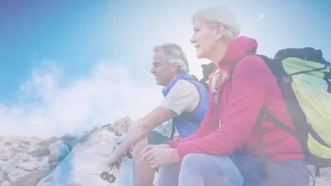 Happy-caucasian-senior-couple-hiking-in-mountains-over-fast-moving-clouds