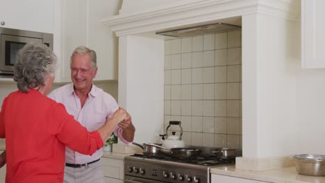 Happy-caucasian-senior-couple-having-fun-smiling-and-dancing-in-kitchen