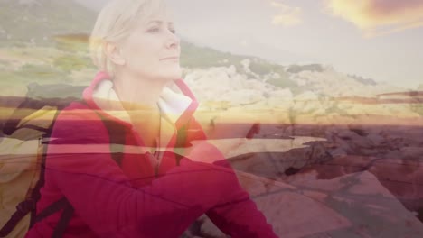 Caucasian-senior-woman-hiking-sitting-on-rocks-relaxing,-over-moving-clouds-and-sunset