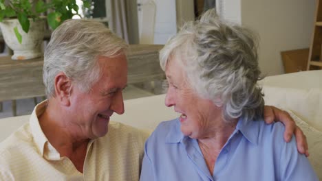 Kaukasisches-älteres-Paar-Lächelt,-Während-Es-Sich-Gegenseitig-Ansieht,-Während-Es-Zu-Hause-Auf-Der-Couch-Sitzt