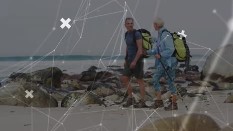 Caucasian-senior-couple-hiking-by-the-sea,-over-moving-network-of-connections