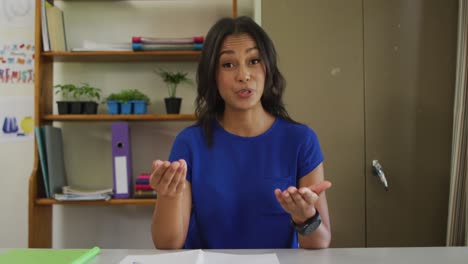 Mixed-race-female-teacher-sitting-at-desk-having-video-call