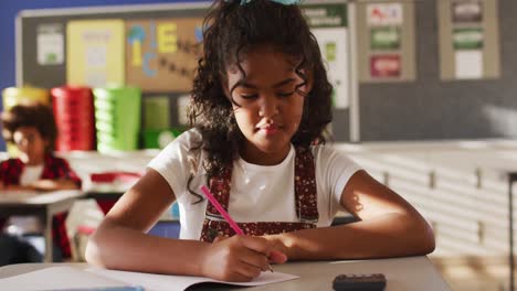 Portrait-of-mixed-race-schoolgirl-sitting-in-class,-making-notes,-looking-at-camera