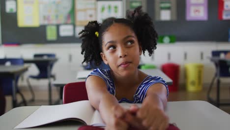 Portrait-of-happy-mixed-race-schoolgirl-sitting-at-classroom,-answering-question,-looking-at-camera