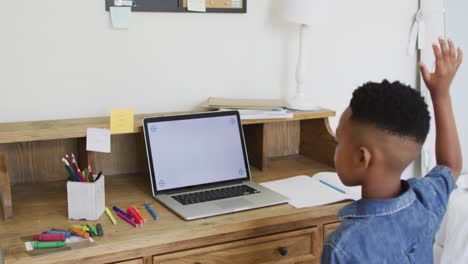 African-american-boy-at-home-in-online-school-class-raising-hand-using-laptop-copy-space-on-screen