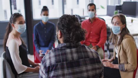 Diverse-group-of-business-colleagues-wearing-face-masks-discussing