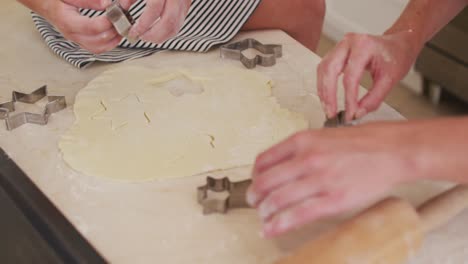 Mid-section-of-mother-and-daughter-cutting-the-dough-with-baking-tin-in-star-shapes-in-the-kitchen