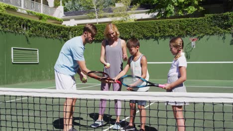 Caucasian-father-and-mother-teaching-their-kids-to-play-tennis-at-tennis-court-on-a-bright-sunny-day