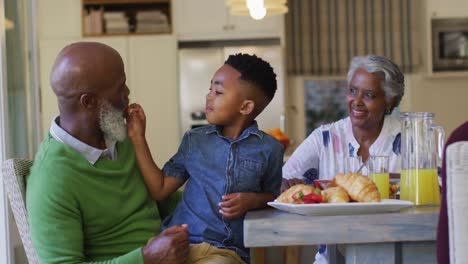 Afroamerikanischer-Junge-Füttert-Seinen-Großvater-Mit-Erdbeeren,-Während-Er-Zu-Hause-Auf-Seinem-Schoß-Sitzt