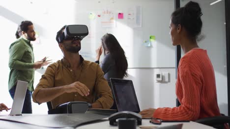 Diverse-group-of-business-colleagues-talking-and-using-vr-headset-in-a-meeting-room