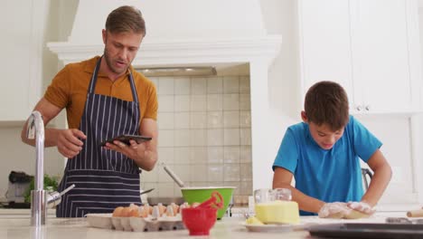 Kaukasischer-Vater-Und-Sohn-Nutzen-Ein-Digitales-Tablet-Und-Backen-Gemeinsam-In-Der-Küche-Zu-Hause