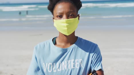 Porträt-Einer-Afroamerikanischen-Frau-Mit-Freiwilligen-T-Shirt-Und-Gesichtsmaske,-Die-In-Die-Kamera-Blickt