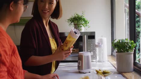 Asian-mother-and-daughter-preparing-healthy-drink-in-kitchen-smiling