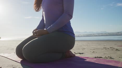 Mixed-race-woman-meditating-on-yoga-mat-at-the-beach
