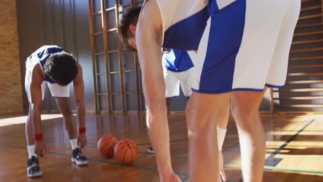 Vielfältiges-Männliches-Basketballteam,-Das-Blaue-Sportkleidung-Trägt-Und-Sich-Dehnt