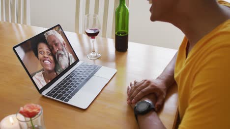 Mid-section-of-african-american-man-talking-on-video-call-on-laptop-at-home