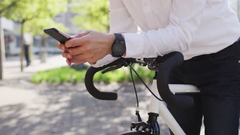 Mid-section-of-man-using-smartphone-while-leaning-on-his-bicycle-on-the-street