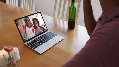 Mid-section-of-african-american-man-drinking-wine-while-having-a-video-call-on-laptop-at-home