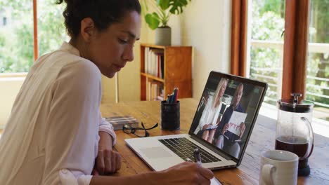 African-american-woman-taking-notes-while-having-a-video-call-on-laptop-at-home