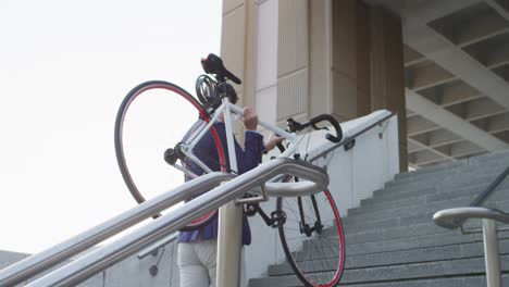 Hombre-Asiático-Con-Mascarilla-Llevando-Bicicleta-Mientras-Subía-Las-Escaleras-En-El-Parque-Corporativo