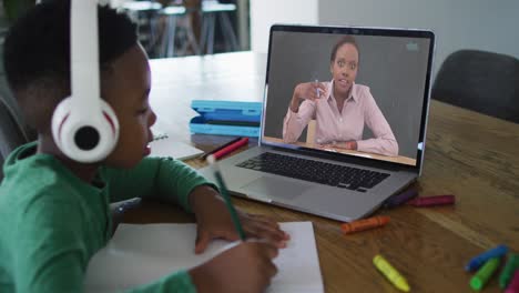Afroamerikanischer-Junge-Mit-Kopfhörern,-Der-Einen-Videoanruf-Auf-Dem-Laptop-Führt,-Während-Er-Zu-Hause-Hausaufgaben-Macht