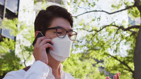 Asiatischer-Mann-Mit-Gesichtsmaske,-Der-Auf-Der-Straße-Mit-Dem-Smartphone-Spricht