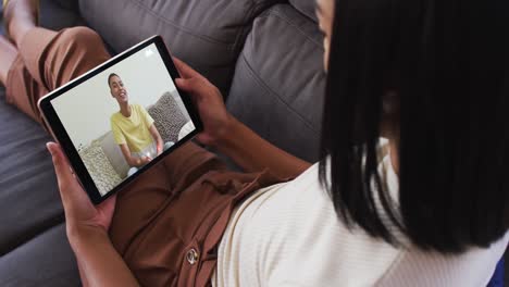 Mujer-Afroamericana-Haciendo-Una-Videollamada-En-Una-Tableta-Digital-Mientras-Está-Sentada-En-El-Sofá-De-Casa