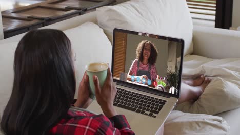 Afroamerikanische-Frau-Hält-Eine-Kaffeetasse-In-Der-Hand-Und-Führt-Einen-Videoanruf-Auf-Dem-Laptop,-Der-Zu-Hause-Auf-Der-Couch-Sitzt