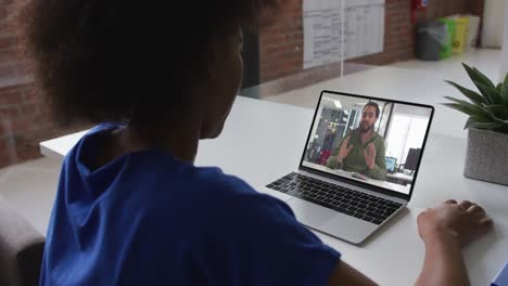 African-american-woman-talking-on-video-call-with-male-colleague-on-laptop-at-office