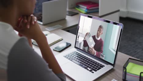 Mid-section-of-african-american-woman-having-a-video-call-on-laptop-with-male-colleague-at-office