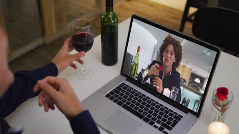 Mid-section-of-african-american-woman-holding-wine-glass-while-having-a-video-call-on-laptop-at-home